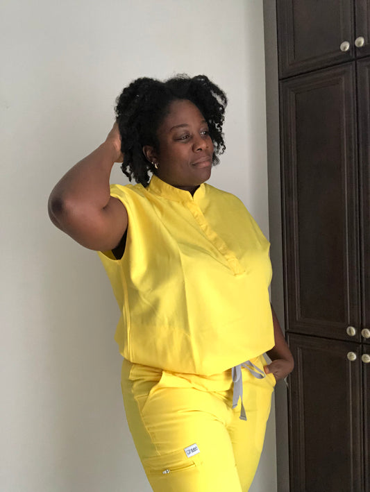 Black woman weary yellow nursing scrub close to a dark brown cupboard